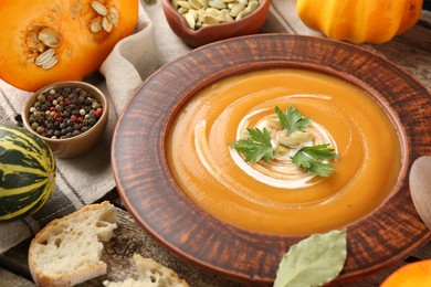 Photo of Delicious pumpkin soup with seeds and parsley in bowl on wooden table, closeup
