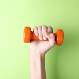 Woman holding vinyl dumbbell on color background, closeup