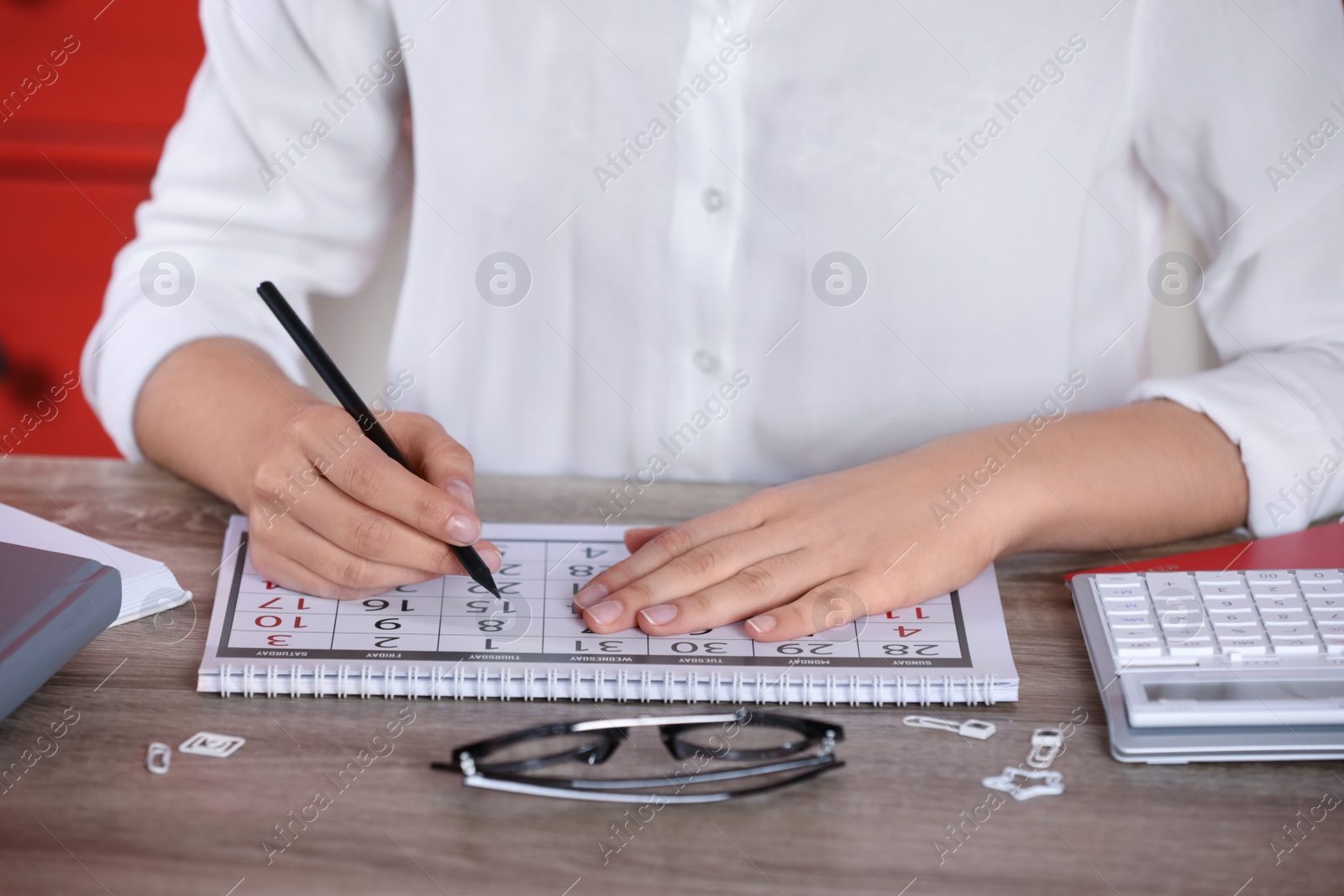 Photo of Woman marking date in calendar at wooden table, closeup