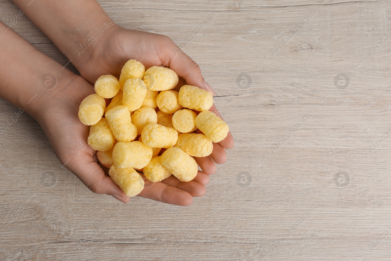 Photo of Woman holding corn sticks at wooden table, top view