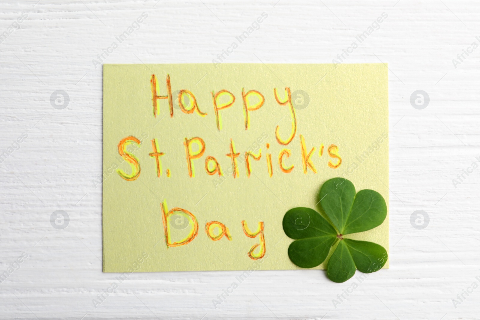 Photo of Clover leaf and note with text HAPPY ST. PATRICK'S DAY on white wooden table, flat lay