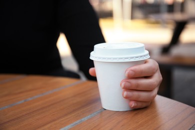 Woman with cardboard cup of coffee at table outdoors, closeup