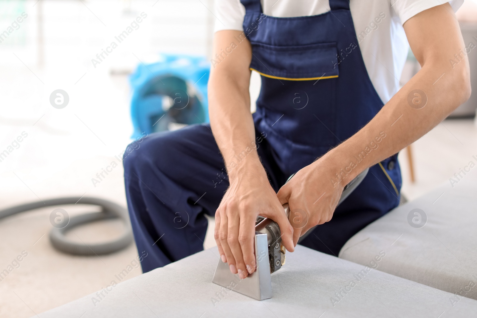 Photo of Dry cleaning worker removing dirt from sofa indoors