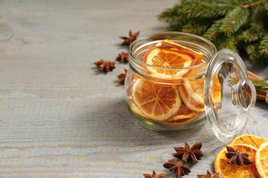 Photo of Glass jar with dry orange slices and anise stars on grey wooden table. Space for text