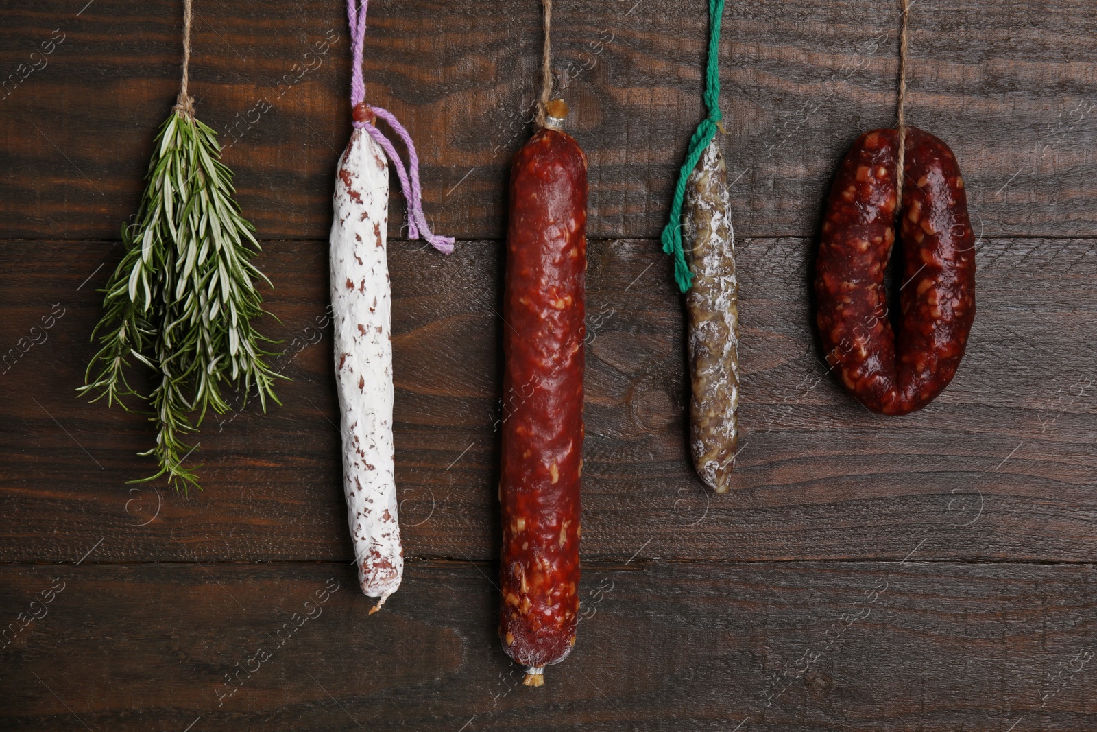 Photo of Different delicious sausages and bunch on rosemary hanging near wooden wall