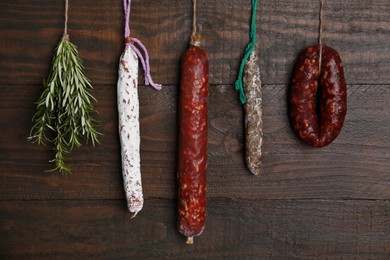 Different delicious sausages and bunch on rosemary hanging near wooden wall
