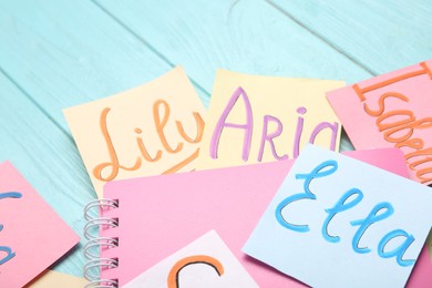 Photo of Paper notes with different baby names and notebook on light blue wooden table, closeup