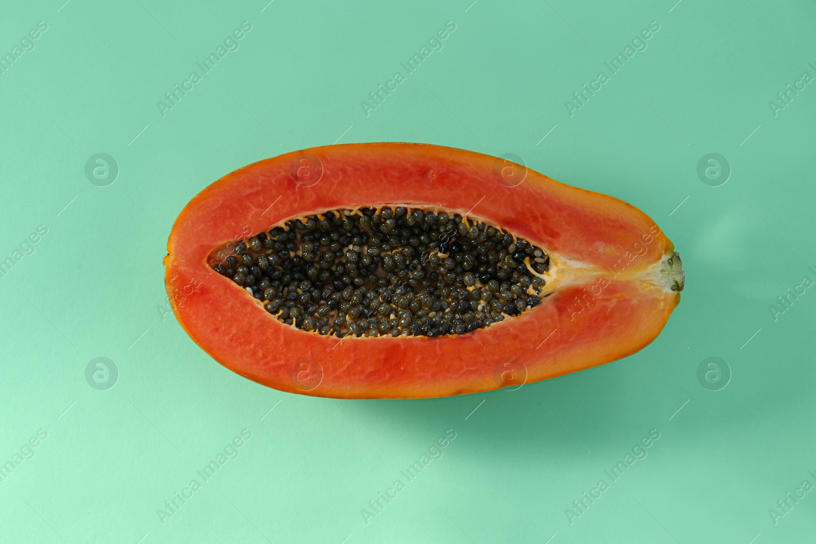 Photo of Half of fresh ripe papaya on light turquoise background, top view. Exotic fruit