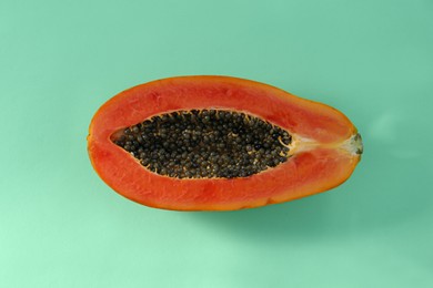 Photo of Half of fresh ripe papaya on light turquoise background, top view. Exotic fruit