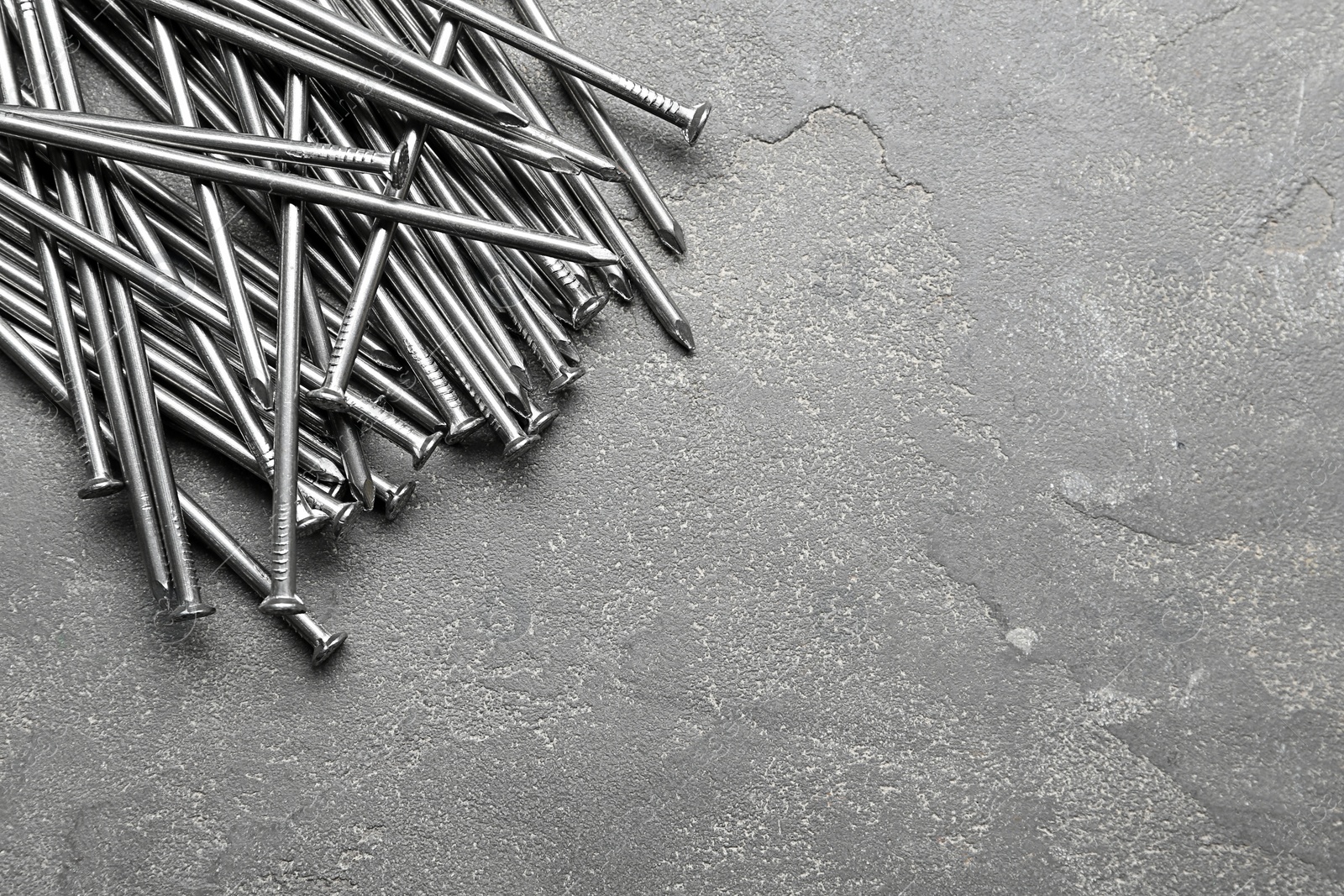 Photo of Pile of metal nails on grey stone background, flat lay. Space for text