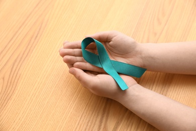 Photo of Woman holding teal awareness ribbon on wooden background, closeup