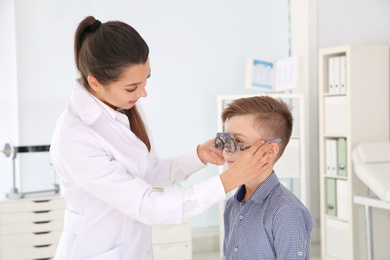 Photo of Children's doctor putting trial frame on little boy in clinic. Eye examination