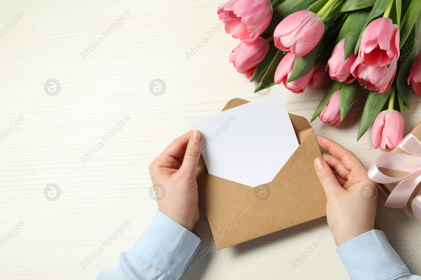 Photo of Happy Mother's Day. Woman holding envelope with blank card at white wooden table, top view. Space for text