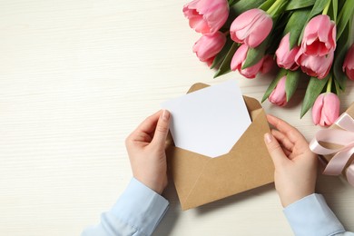 Photo of Happy Mother's Day. Woman holding envelope with blank card at white wooden table, top view. Space for text