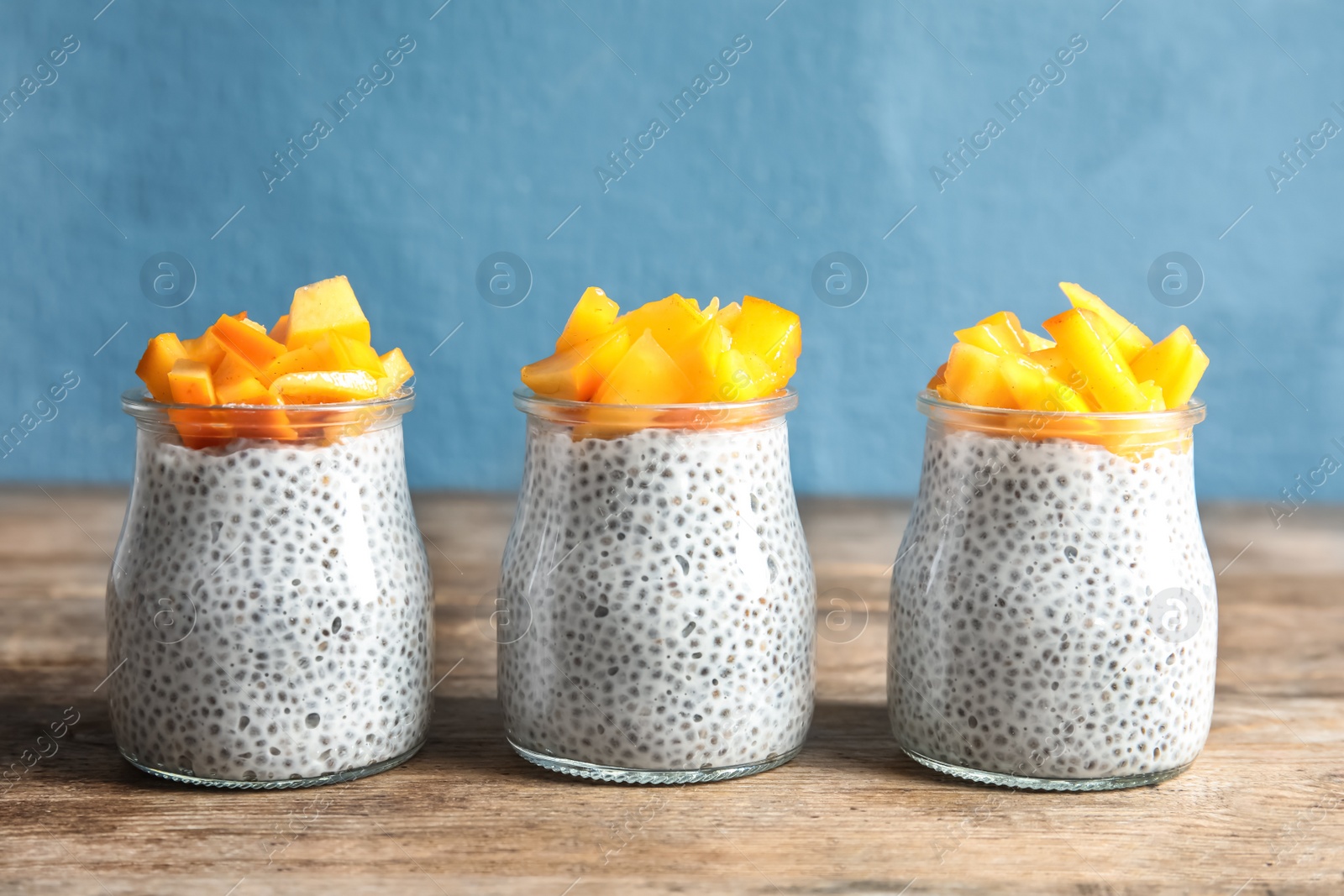 Photo of Jars of tasty chia seed pudding with persimmon on table