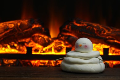 Photo of Cute decorative snowman on wooden floor near fireplace, space for text