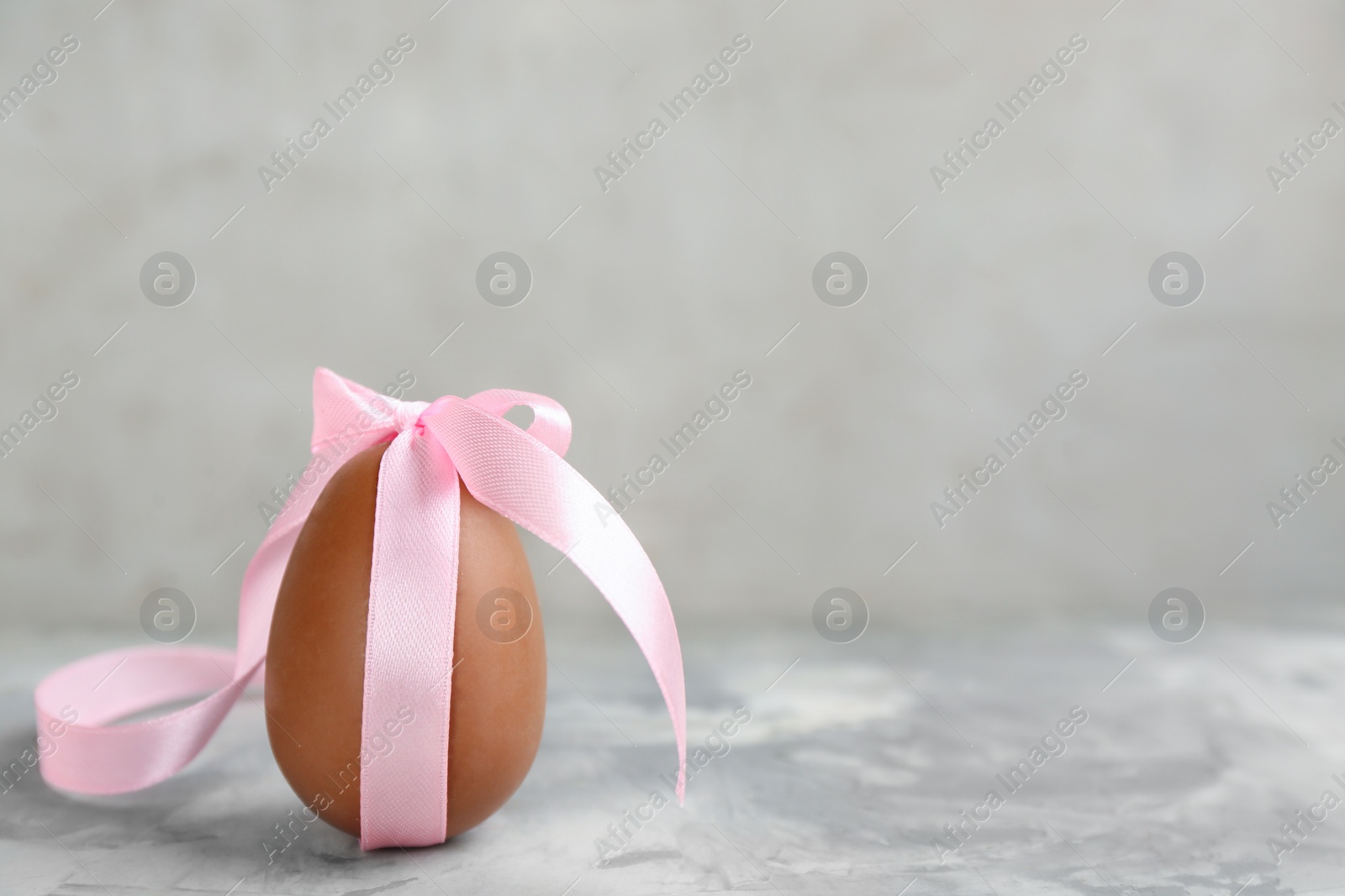 Photo of Sweet chocolate egg with pink bow on grey marble table. Space for text