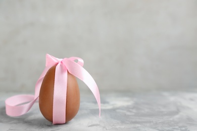 Photo of Sweet chocolate egg with pink bow on grey marble table. Space for text