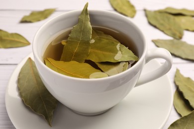 Cup of freshly brewed tea with bay leaves on white wooden table, closeup