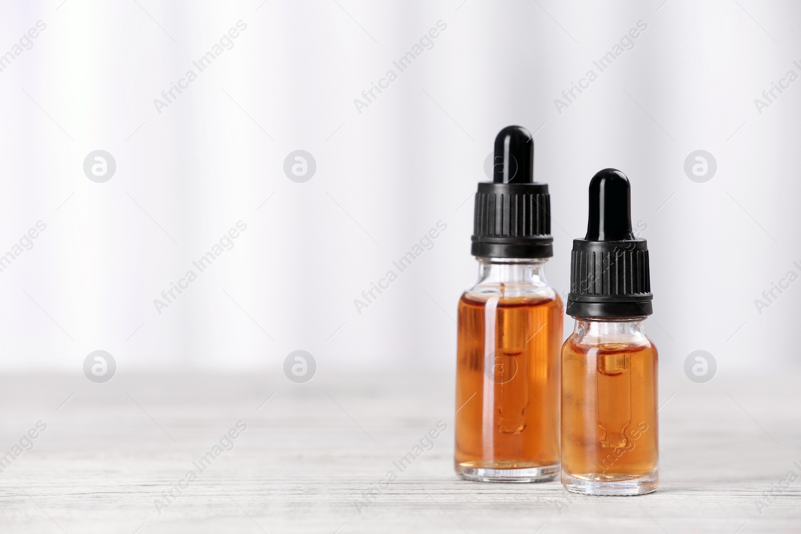 Photo of Bottles of essential oils on table against light background, space for text. Cosmetic products