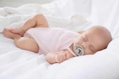 Cute little baby with pacifier sleeping on bed