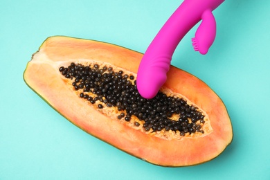 Half of papaya and purple vibrator on turquoise background, top view. Sex concept