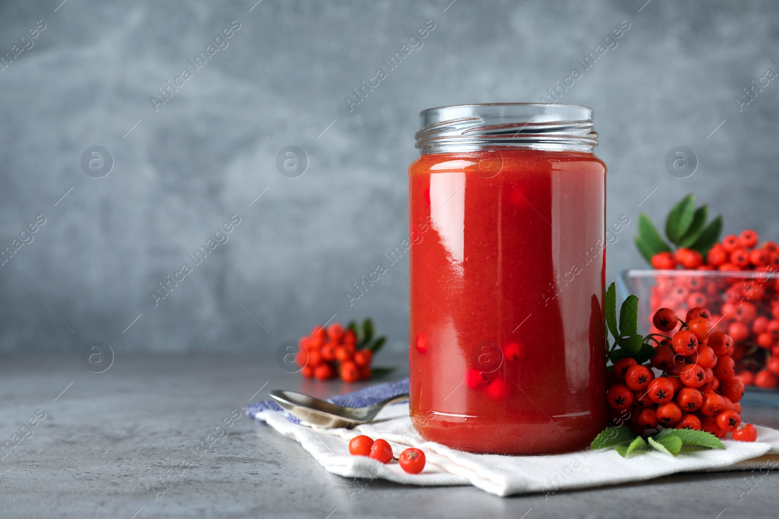 Photo of Delicious rowan jam in glass jar on grey table. Space for text