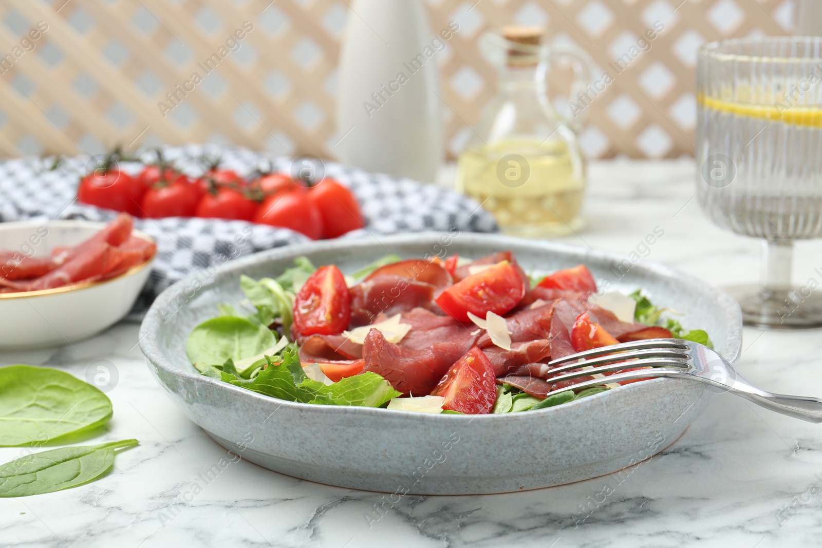 Photo of Delicious bresaola salad with tomatoes and parmesan cheese served on white marble table, closeup