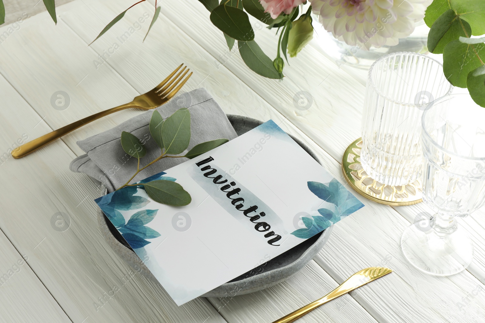 Photo of Card with word Invitation, cutlery and glasses on white wooden table