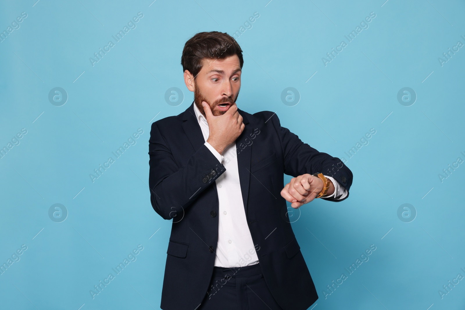 Photo of Emotional man checking time on light blue background. Being late concept