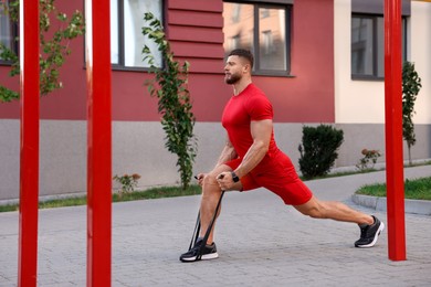 Photo of Muscular man doing exercise with elastic resistance band on sports ground