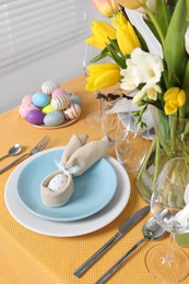 Photo of Festive table setting with painted eggs, plate and vase of tulips. Easter celebration