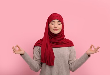 Photo of Muslim woman in hijab meditating on pink background
