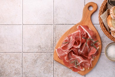 Photo of Slices of tasty cured ham, bread and rosemary on tiled table, flat lay. Space for text