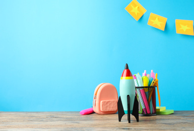 Photo of Bright toy rocket and school supplies on wooden table. Space for text