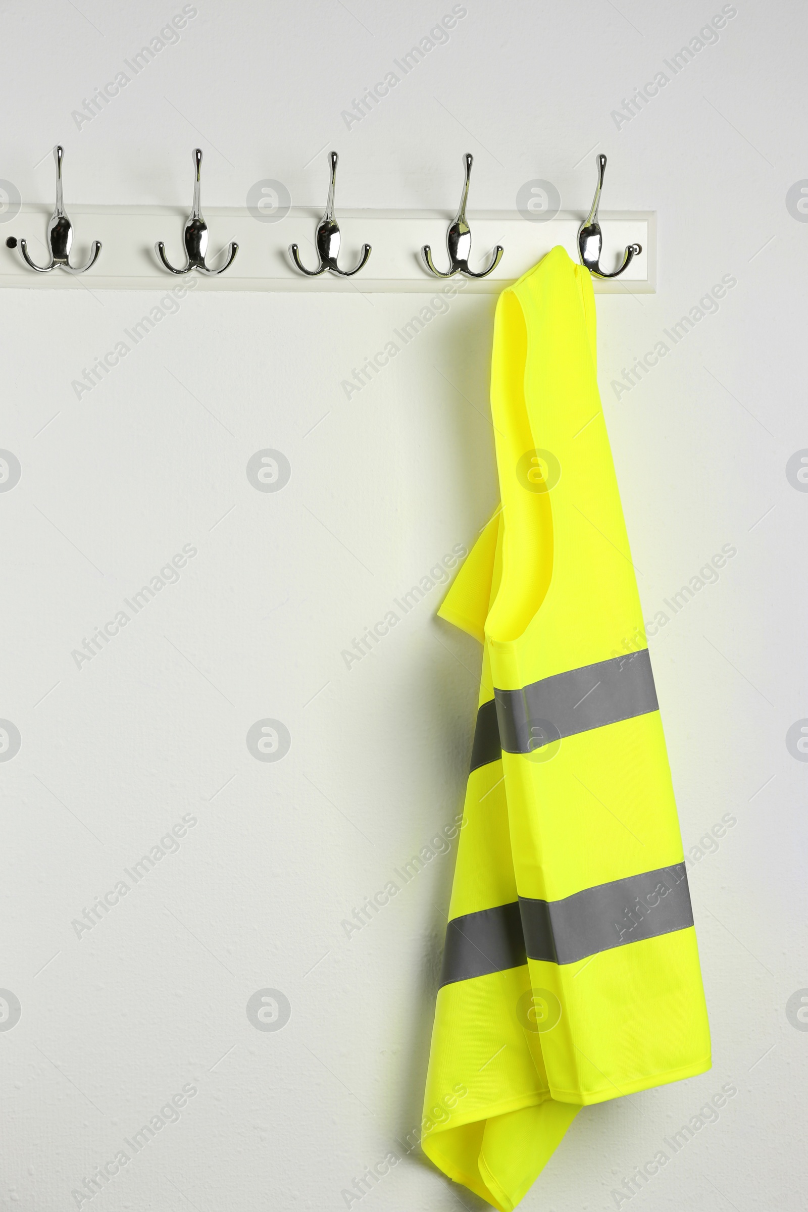 Photo of Reflective vest hanging on white wall. Safety equipment