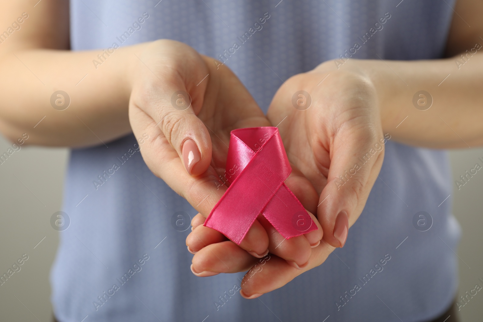 Photo of Woman with pink ribbon on light grey background, closeup. Breast cancer awareness