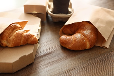 Paper bags with pastry and takeaway food on wooden table