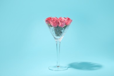 Beautiful martini glass with pink roses on light blue background