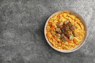 Photo of Delicious pilaf with meat on grey textured table, top view. Space for text