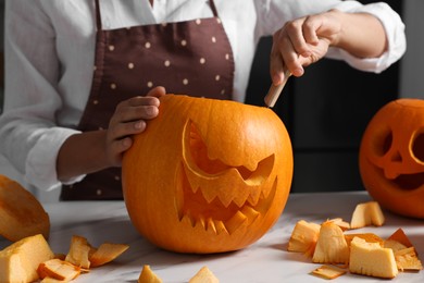 Photo of Woman carving pumpkin for Halloween at white marble table, closeup