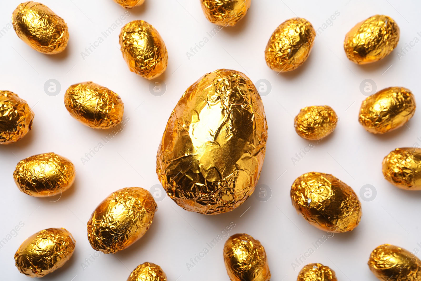 Photo of Chocolate eggs wrapped in golden foil on white background, flat lay