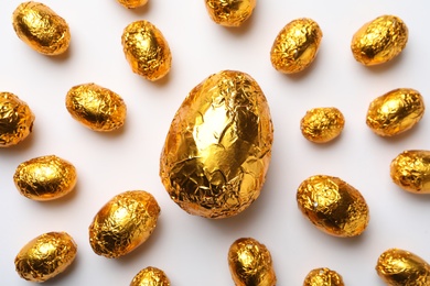 Photo of Chocolate eggs wrapped in golden foil on white background, flat lay