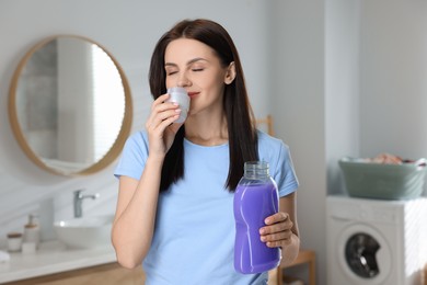 Photo of Beautiful woman smelling fabric softener in bathroom