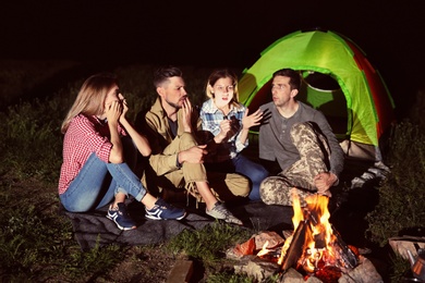 Photo of Woman with flashlight telling scary story for her friends near bonfire at night. Camping season