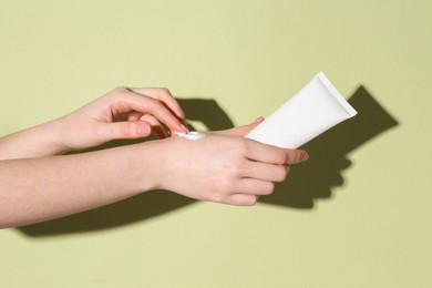 Woman with tube applying cream on her hand against green background, closeup