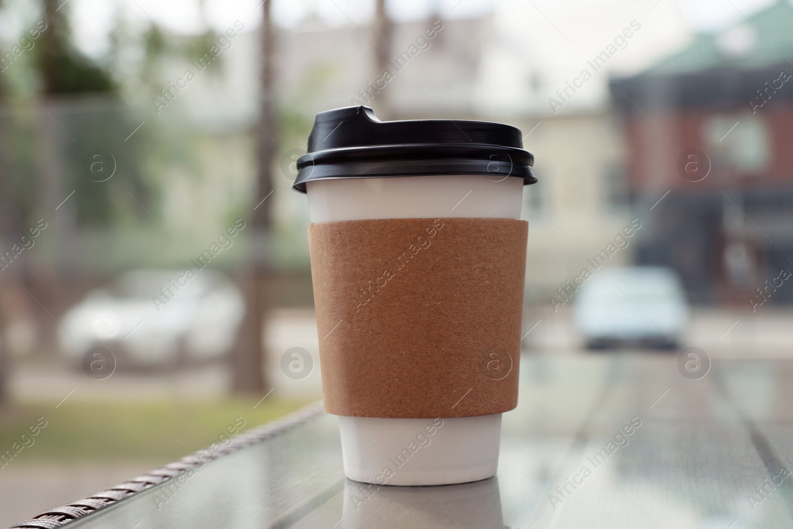 Photo of Paper takeaway cup on glass table outdoors. Coffee to go