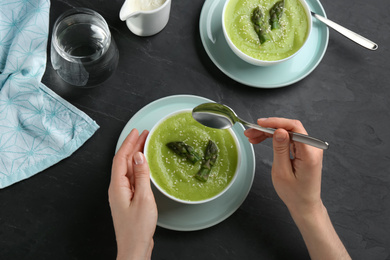 Woman eating delicious asparagus soup at black table, top view