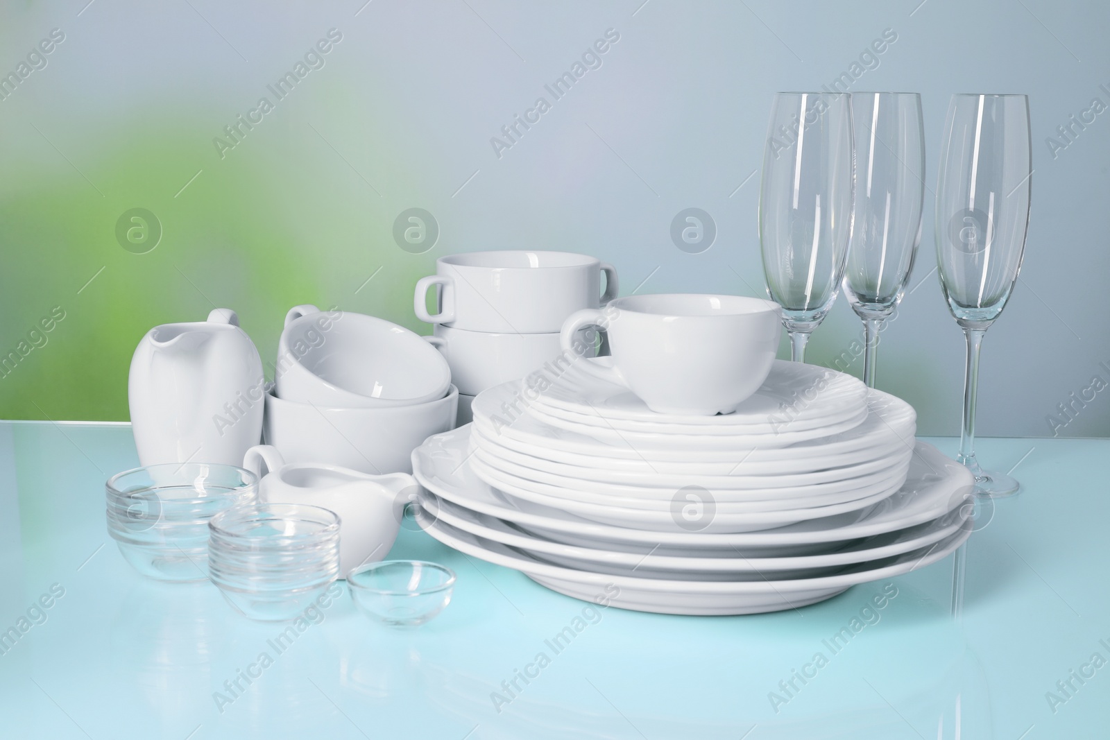 Photo of Set of clean dishes and glasses on light blue table