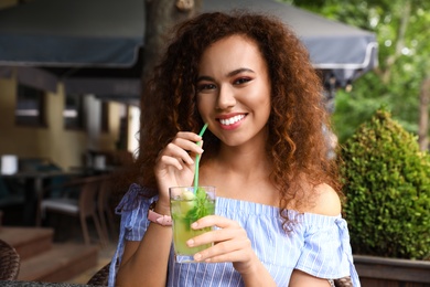 Happy African-American woman with glass of natural lemonade in cafe. Detox drink